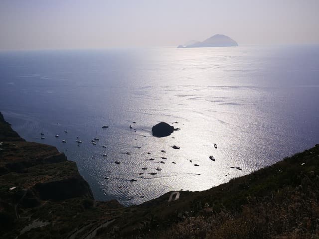 Veduta panoramica dell’isola di Salina con barche ormeggiate lungo la costa e il mare che riflette la luce del sole.
