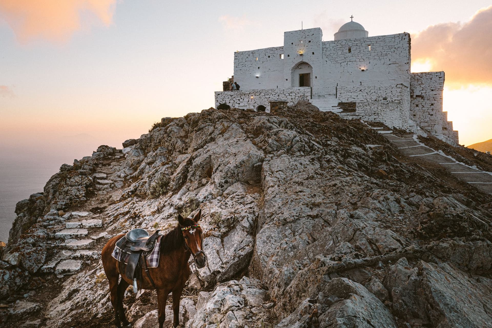 A donkey with a saddle foregrounds a beautiful monastery in Sifnos, Greece.