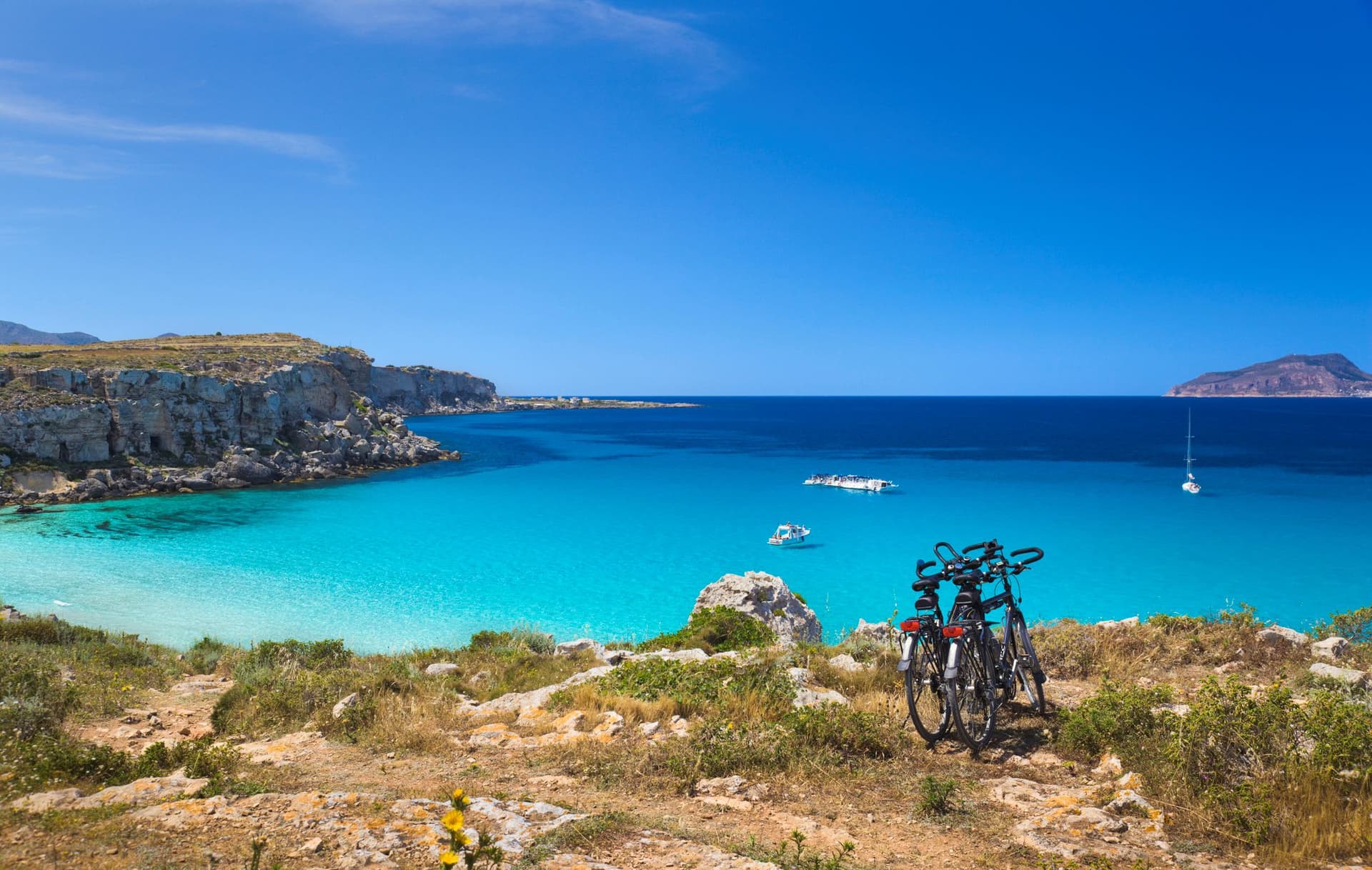 Two bikes rest on the rocky shoreline of Favignana, Italy.