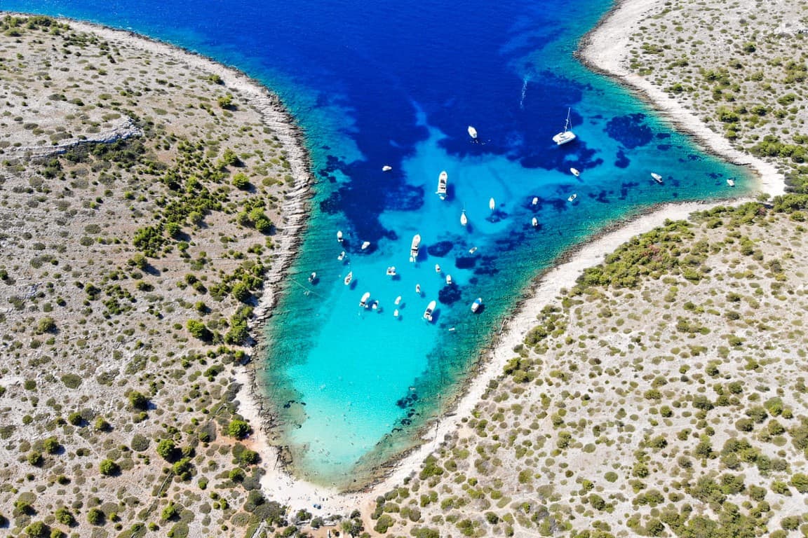 Uvala s tirkiznim morem i usidrenim jedrilicama okružena kršom u Nacionalnom parku Kornati, Hrvatska.