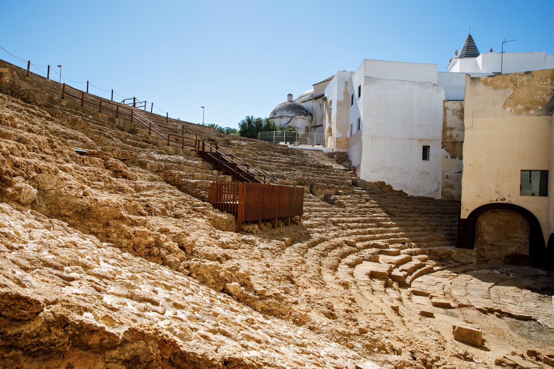 Un théâtre romain proche de constructions modernes sous un ciel bleu.