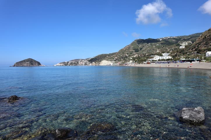 La spiaggia dei Maronti a Ischia con acqua cristallina, costa ampia e colline verdi sullo sfondo.