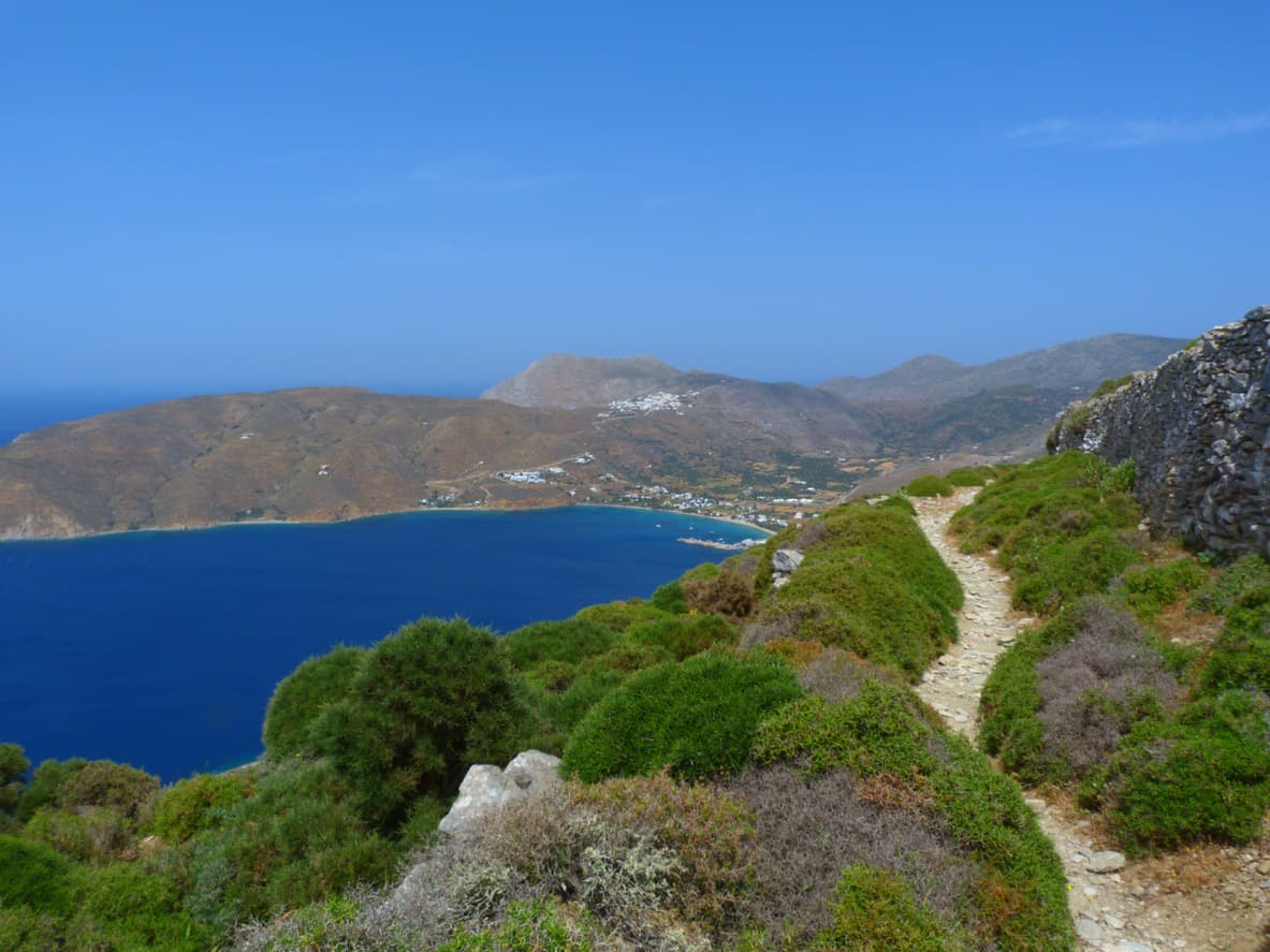 Un chemin de randonnée verdoyant au-dessus d'une falaise surplombant une crique bleu azur