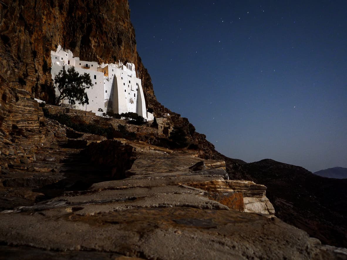 Un ancien monastère blanc incrusté dans la falaise, à la tombée de la nuit