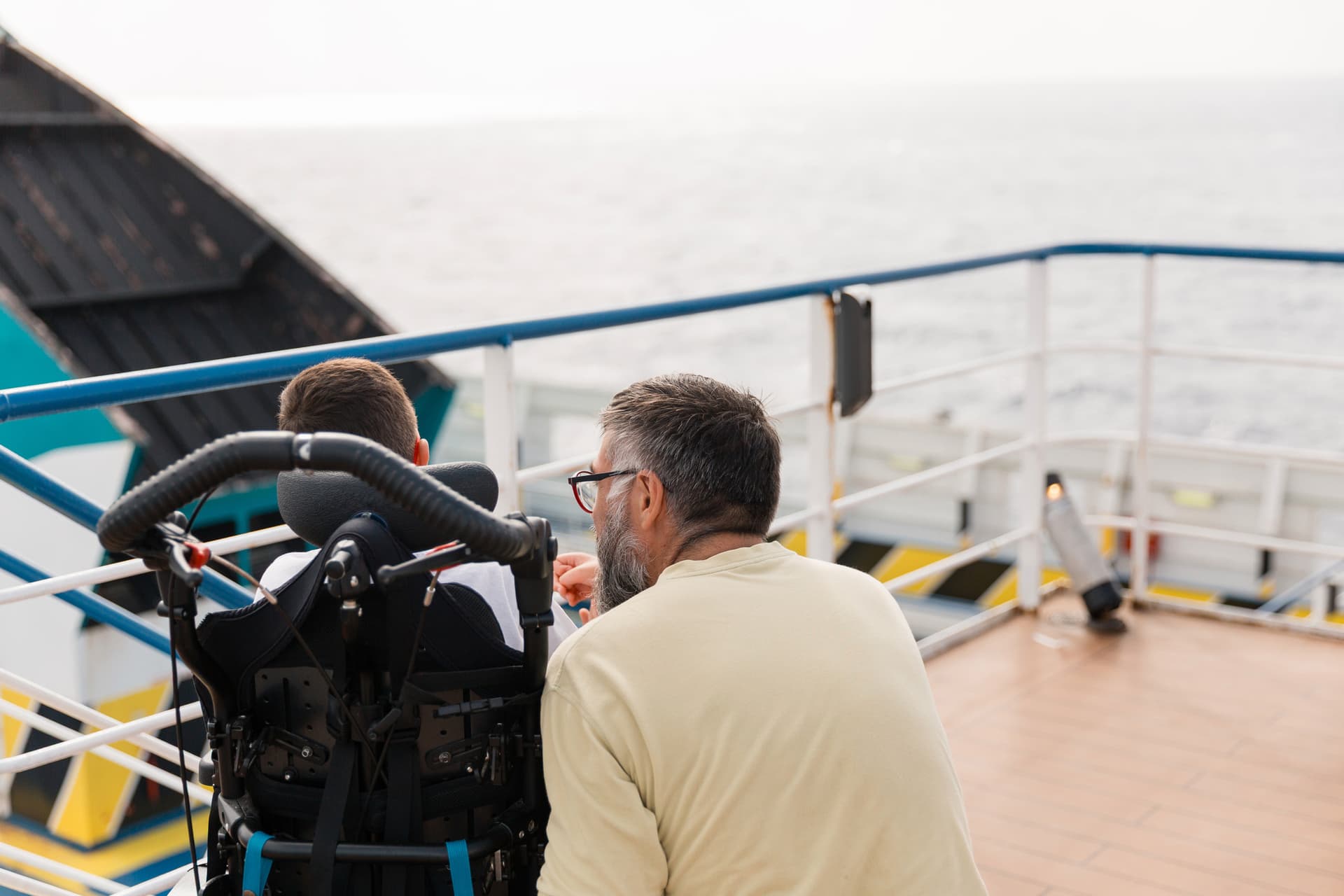 Un enfant en fauteuil roulant profitant de la vue du pont extérieur d'un ferry avec son papa