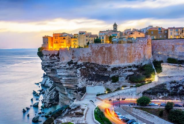 Vista di Bonifacio in Corsica al tramonto con centro storico sulle scogliere bianche affacciate sul mare.