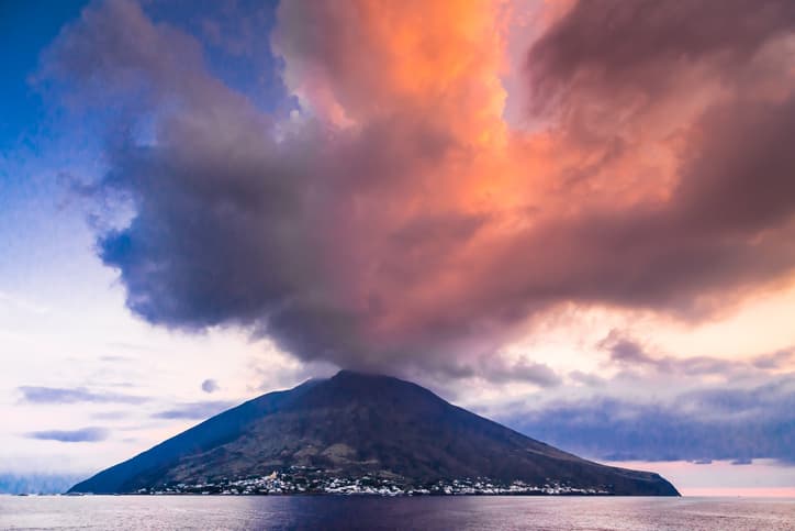 Vulcano di Stromboli al tramonto con pennacchio di fumo e cielo arancione