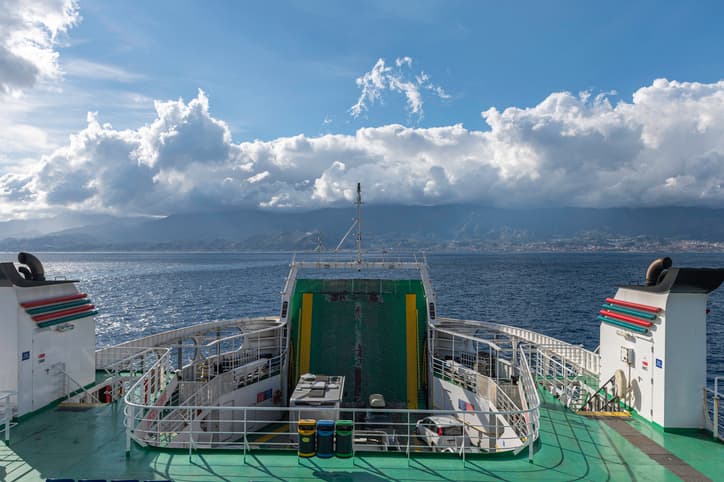 Vista dal ponte di un traghetto in navigazione nello Stretto di Messina con coste montuose sullo sfondo