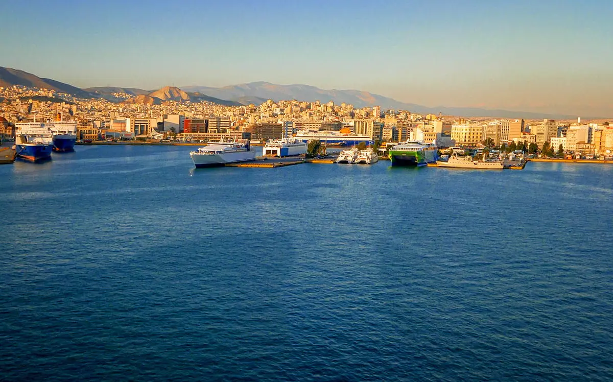 View of a busy ferry port with multiple ships docked along the waterfront of a coastal city.