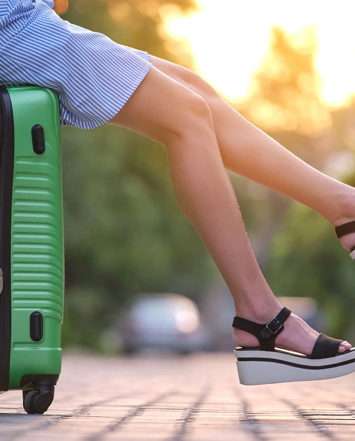Close-up of a traveler sitting on a suitcase next to a parked car, ready to depart.