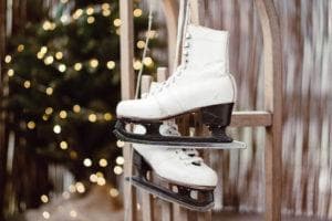pair of white ice skates hanging on wooden ladder with chrismas tree in the background