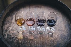 glasses of different colored wine on wooden barrel