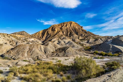 Desert landscape of Tabernas in Almería, Spain, with dry, rugged terrain and sparse vegetation under a bright blue sky.