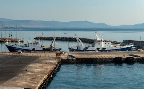 Calm morning at Rafina port with fishing boats docked by the pier and the tranquil Aegean Sea stretching towards the horizon under a clear sky.