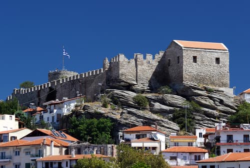 A photo of the stone walls of Kavala Castle in Greece, overlooking the Aegean Sea and a harbor with sailboats.