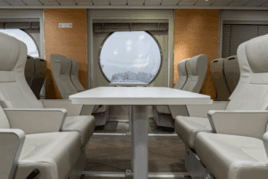 εσωτερικο απο το πλοιο ανεμος της aegean sea lines με λευκα καθισματα τραπεζι στην μεση και μεγαλο στρογγυλο κλειστο παραθυρο στα πλαγια για να βλεπεις το γαλαζιο της θαλασσας κατα την διαρκεια του ταξιδιου