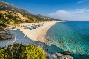 Sunbeds and umbrellas on Dhermi Beach with blue waters at Vlore, Albania