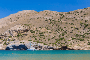 blue and green waters in a beautiful Syros beach and in the depths a boat next to the wild mountain