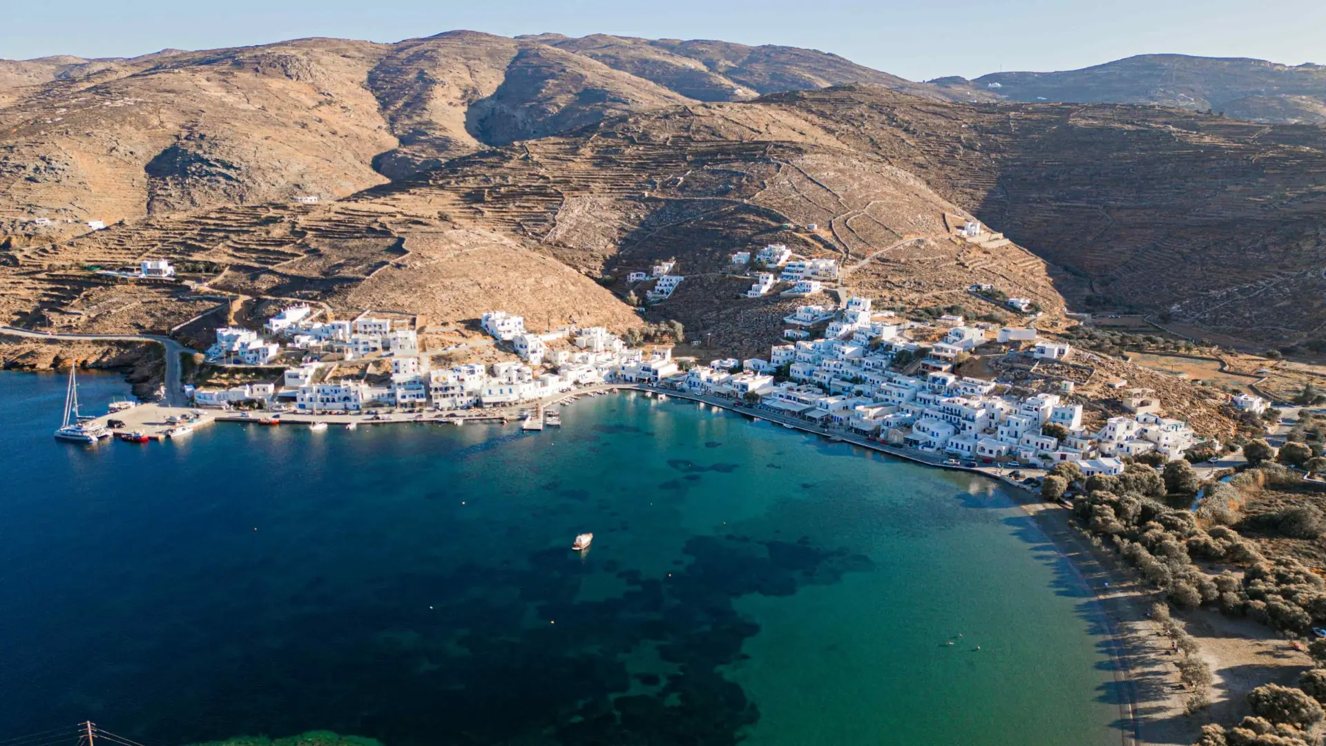 Το γραφικό λιμανάκι της Τήνου ξεπροβάλλει ανάμεσα στα λευκά σπίτια, σε ένα αυθεντικό κυκλαδίτικο σκηνικό.