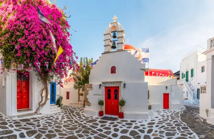 Chiesa bianca di Agia Kyriaki a Mykonos con porte rosse e bouganville fucsia