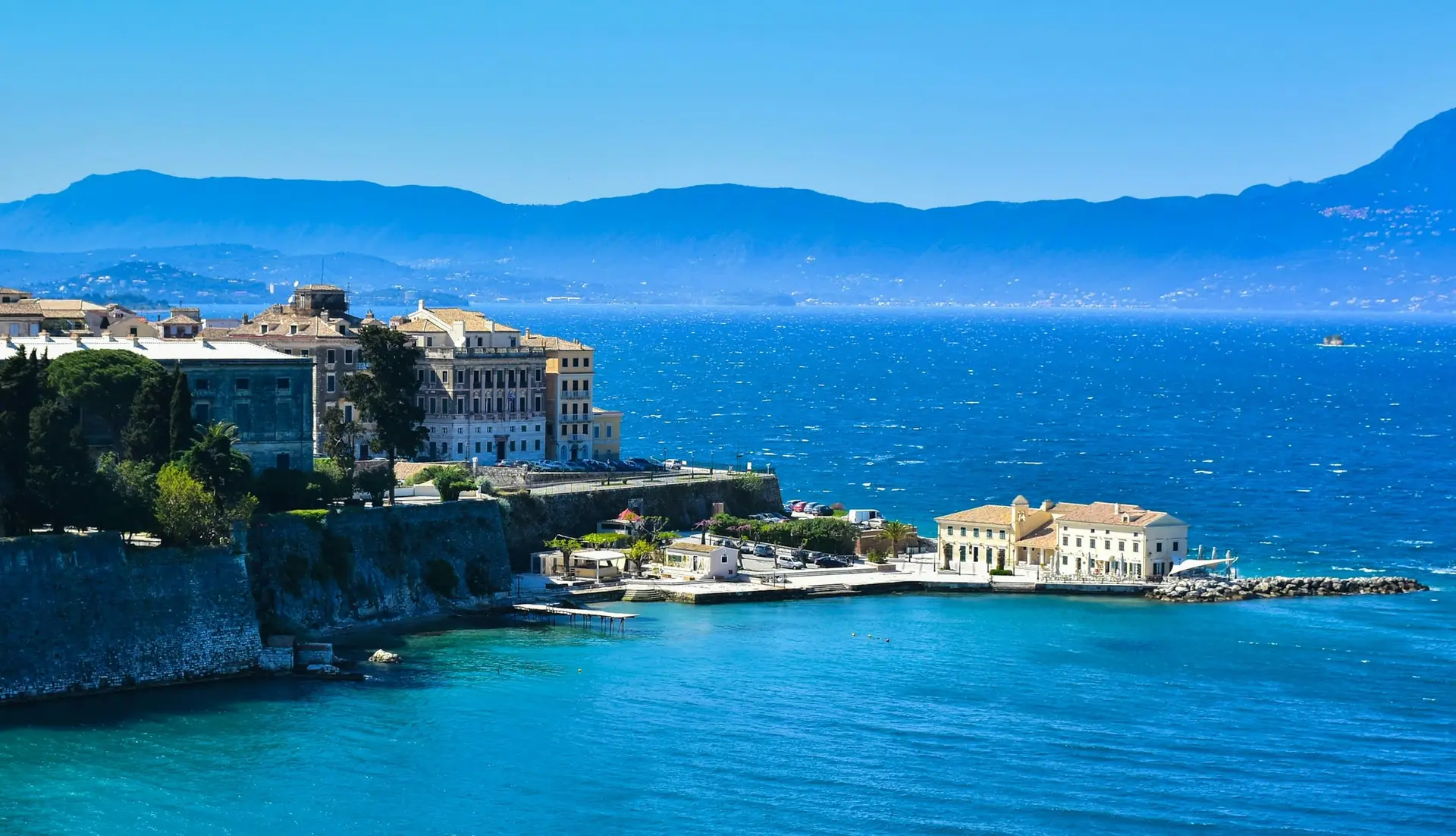 Κέρκυρα Παλιά Πόλη – Εντυπωσιακή ακτογραμμή με ενετικά κτίρια, το φρούριο της πόλης και τη χαρακτηριστική νησίδα με το εκλεκτικό κτήριο του Café En Plo, σε ένα από τα πιο κοσμοπολίτικα νησιά του Ιονίου.