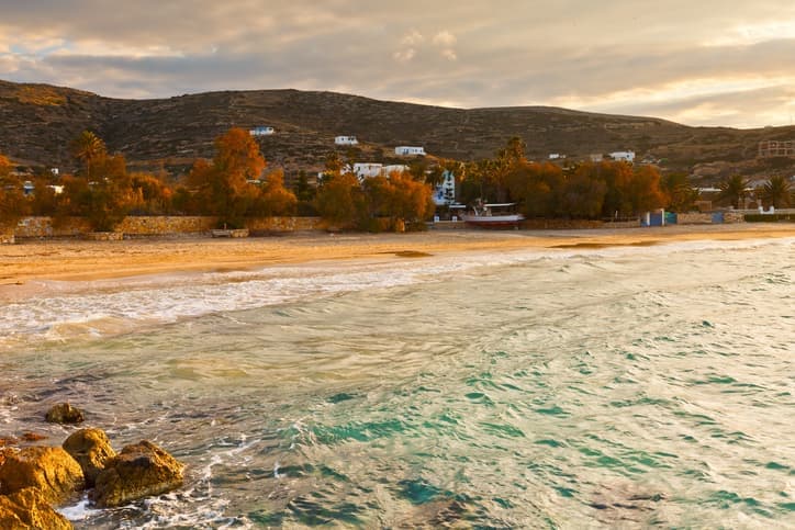 Spiaggia dorata di Donoussa al tramonto con mare cristallino e colline sullo sfondo.