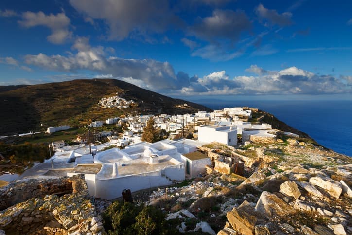 Veduta delle case bianche di Sikinos tra colline e mare sotto un cielo nuvoloso.