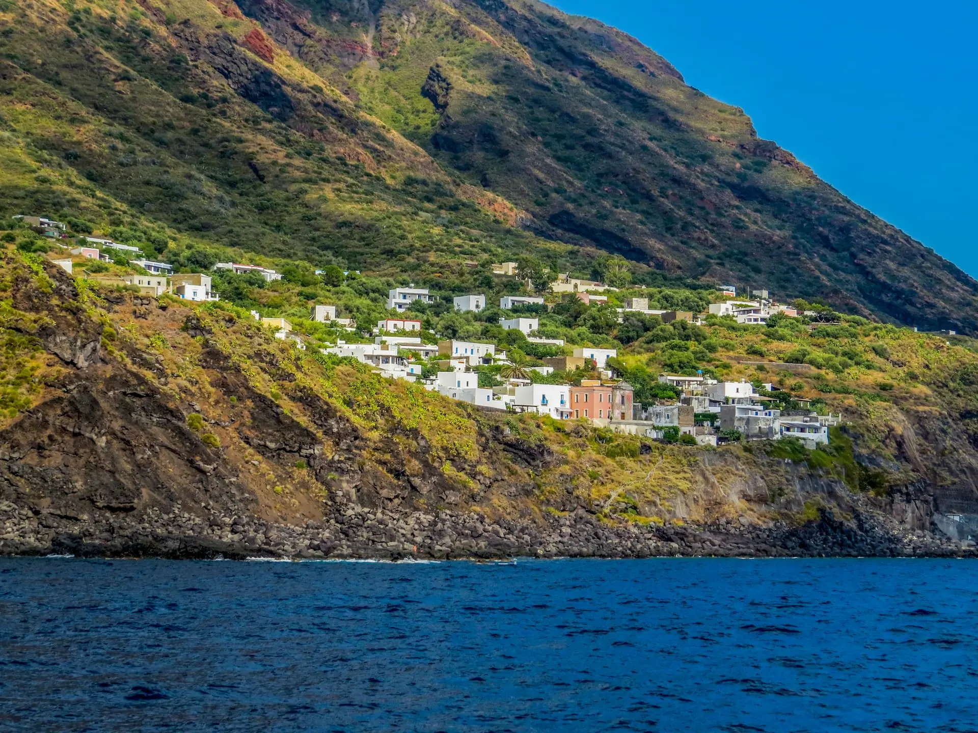 Une vue de Ginostra, un petit village niché sur les falaises escarpées de l'île de Stromboli, en Italie, avec ses maisons blanches disséminées à flanc de colline, surplombant les eaux bleues de la mer Méditerranée.
