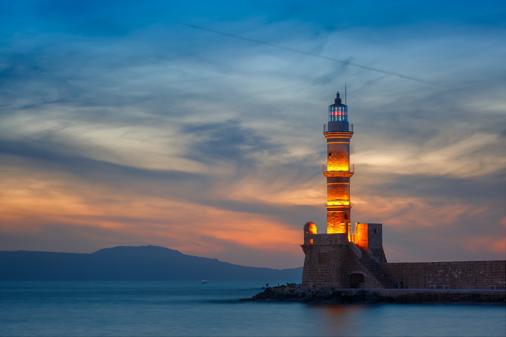 An old lighthouse glows against the sunset in Chania, Crete.