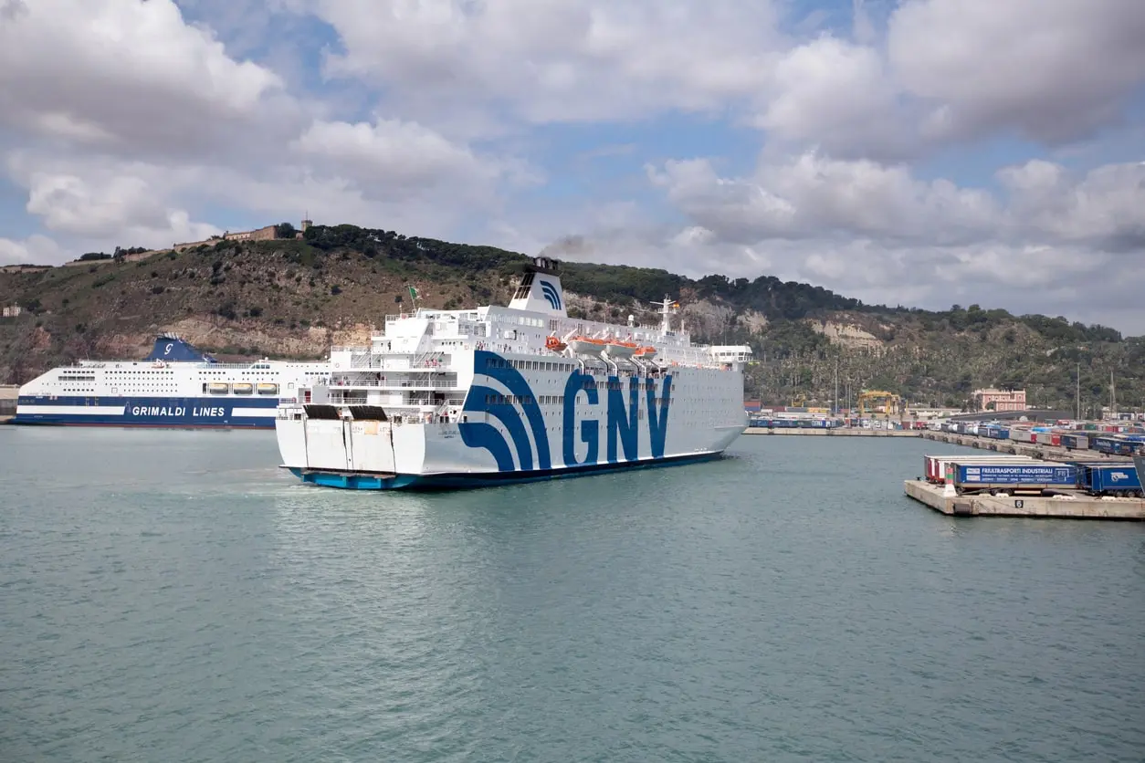 Un ferry de la GNV entrant dans le port de Barcelone, avec en arrière-plan un ferry de la Grimaldi Lines à quai et des conteneurs le long du quai.