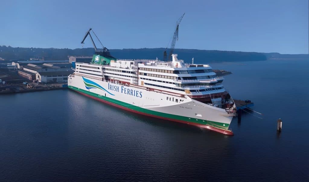 Irish Ferries’ WB Yeats ferry docked at a shipyard, with cranes above and calm waters reflecting the vessel.