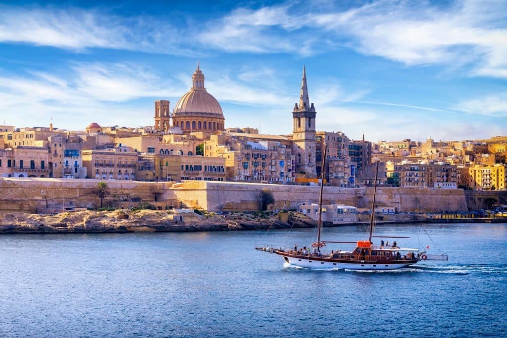 Blick auf Valletta, die Hauptstadt von Malta, mit Kuppel, Kirchturm und einem Segelboot im Vordergrund.