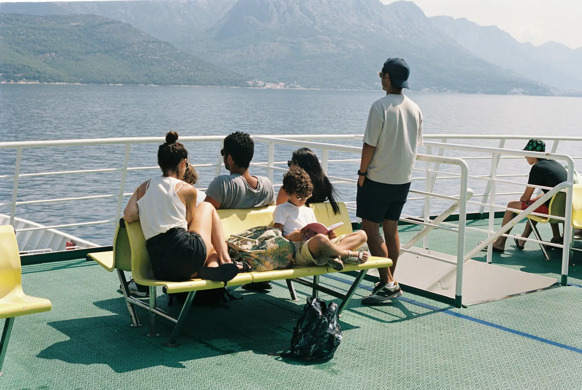 A family sits on the deck of a ferry admiring a beautiful mountain view.