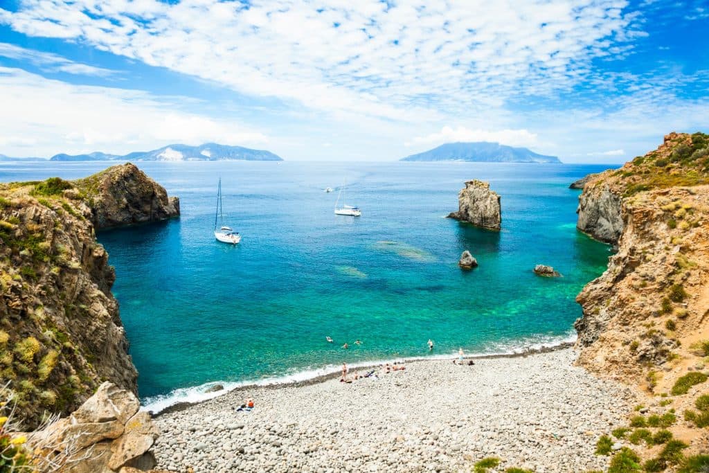 Veduta al tramonto della costa frastagliata di Lipari, isole Eolie, con fichi d’India in primo piano e il mare calmo sullo sfondo.