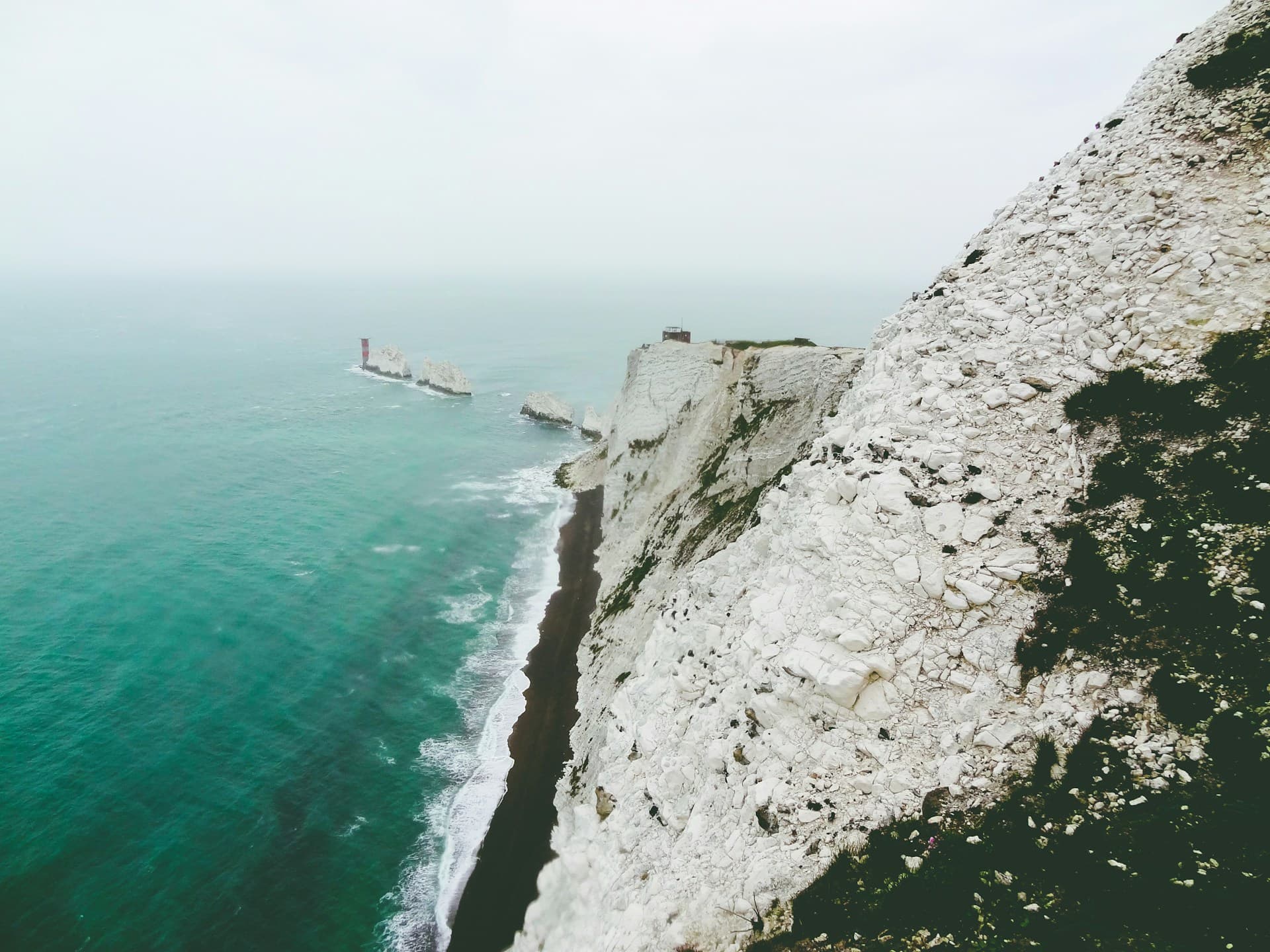 Des rochers pointus et blancs s'élevant de l'eau bleue et troubles devant une falaise.