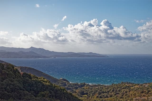 Vista panoramica sulla costa di Nonza, in Corsica settentrionale, con colline verdi e mare profondo sotto un cielo nuvoloso.