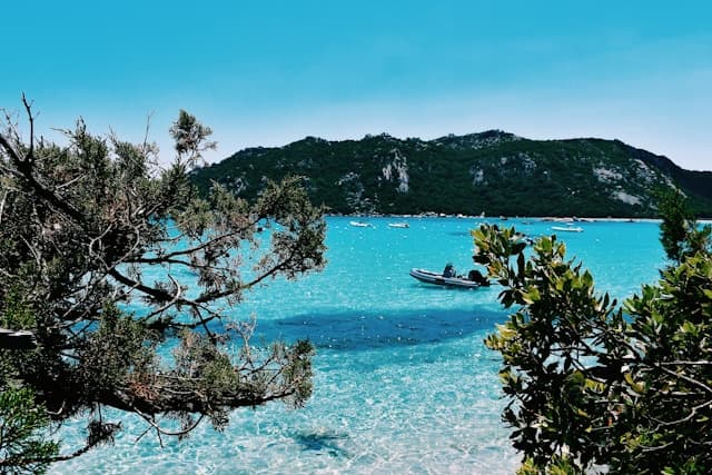 Vista sulla laguna turchese della spiaggia di Santa Giulia in Corsica, con vegetazione in primo piano e barche all’ancora.