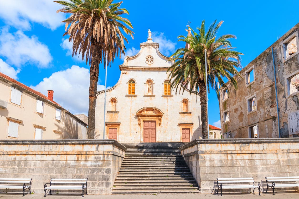 Crkva Gospe od Blagovijesti na otoku Braču u mjestu Milna okružen dvjema palmama.