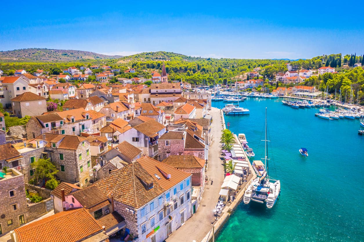 Pogled na marinu i rivu te okolne kamene građevine s crvenim crijepovima u mjestu Milni na otoku Braču iz zraka.