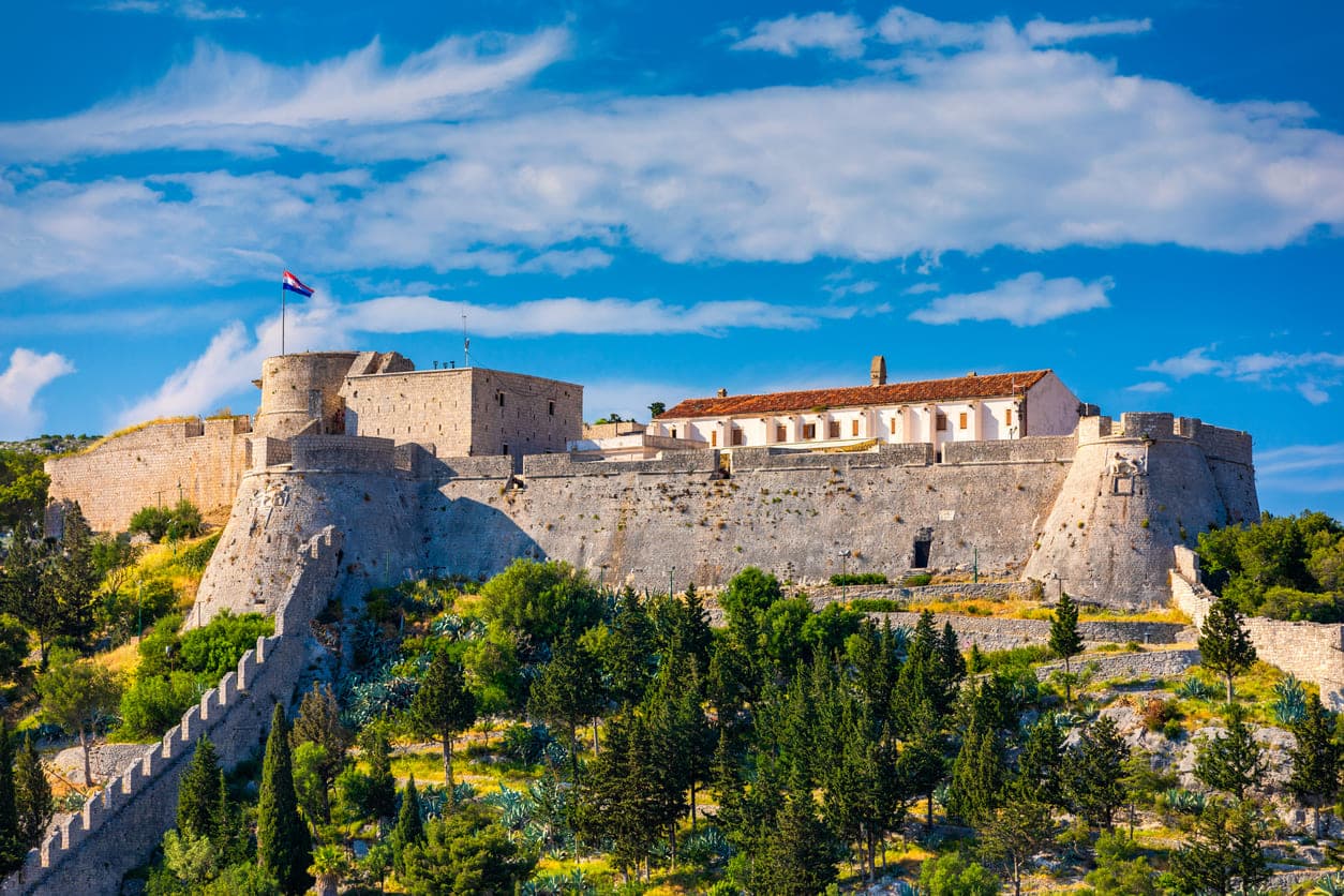 Kamena utvrda Fortica u gradu Hvaru na otoku Hvaru okružena drvećem i plavim nebom.