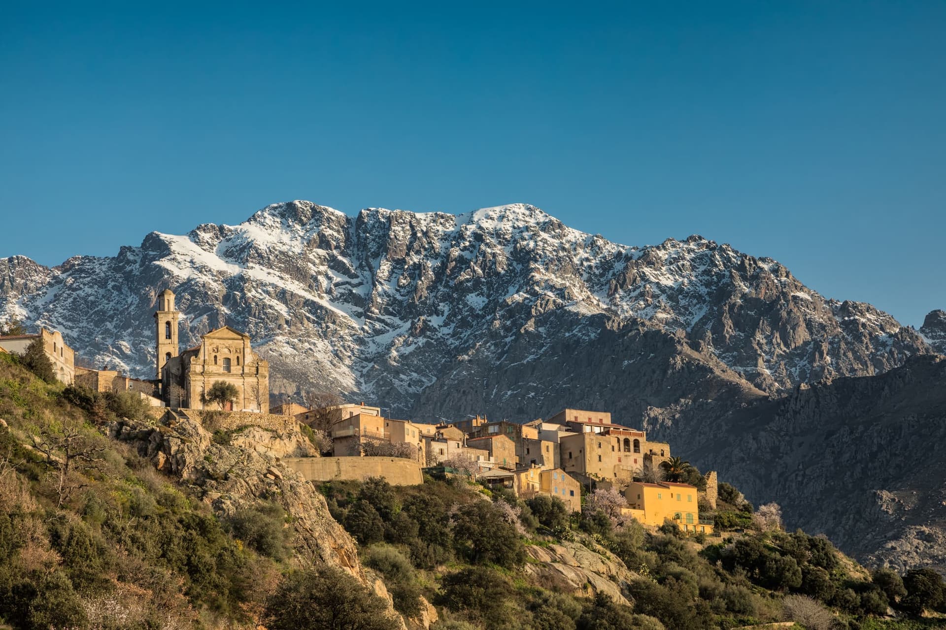 A Medieval castle foregrounds a majestic mountain in Corsica, France.