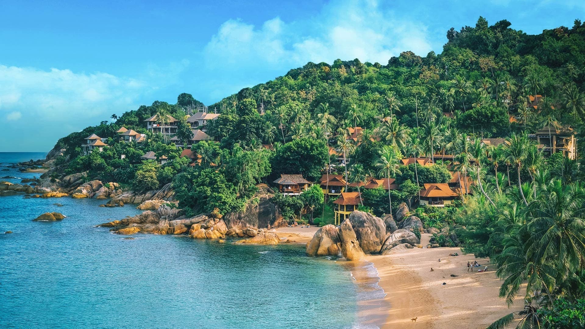 Rustic beachhouses line the lush green coast of Koh Samui, Thailand.