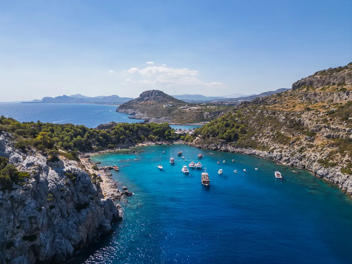 A daytime drone photo of Rhodes. In addition to the blue sea and sky, boats are visible on the water.