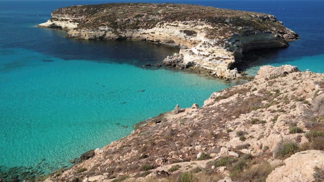 Vista dall’alto della Spiaggia dei Conigli a Lampedusa con acqua turchese e isolotto roccioso di fronte.
