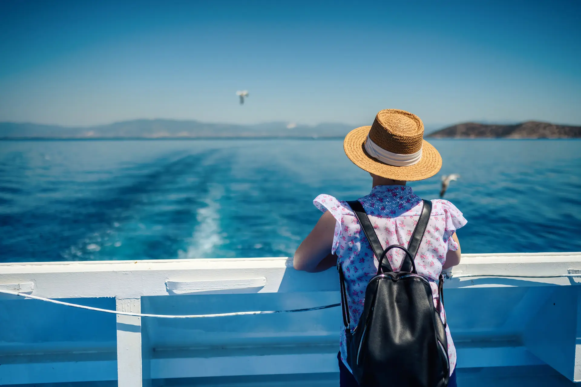 Une femme regarde la mer à l'arrière d'un ferry avec un sac à dos