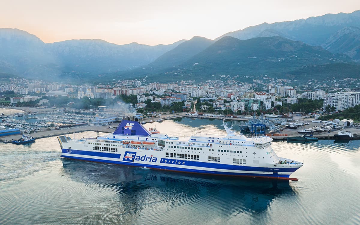 Traghetto Adria Ferries AF Mia in porto al tramonto con città costiera e montagne sullo sfondo