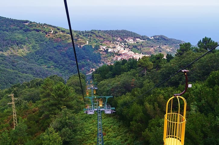 Cabinovia del Monte Capanne con cestello giallo sopra i boschi, con vista sul borgo di Marciana, Isola d'Elba