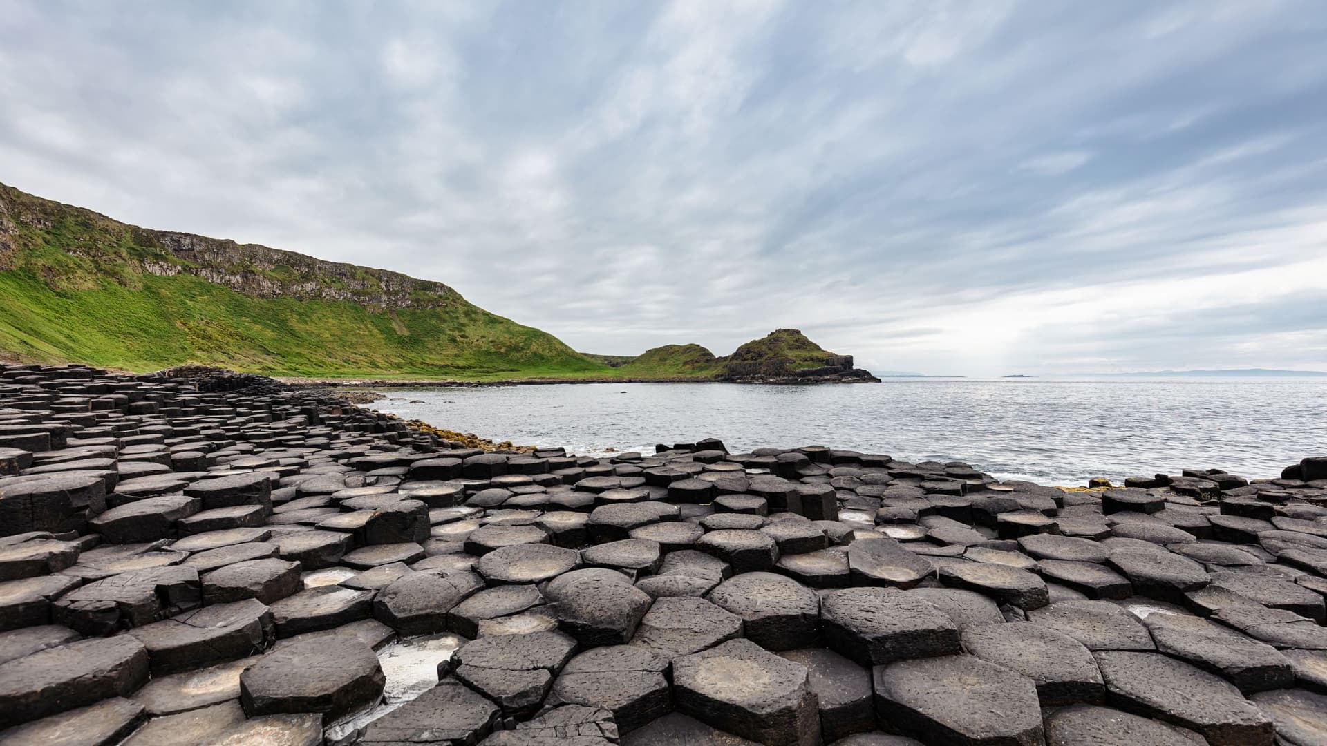 The volcanic stone wonders of the Giants Causeway in Northern Ireland foreground a gloomy shore.