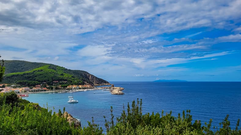 Vista panoramica del porto di Marciana Marina, Isola d'Elba, con la torre sul molo, barche a vela e colline verdi